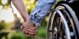 Twee mensen, waarvan één in een rolstoel, houden elkaars hand vast.