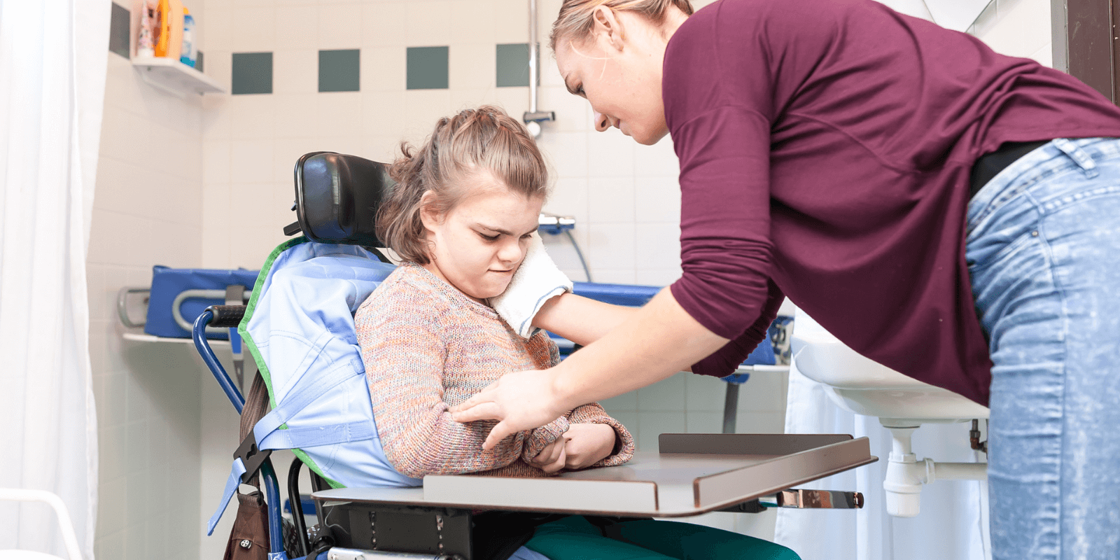 Volwassen vrouw wast meisje in een rolstoel met een washandje