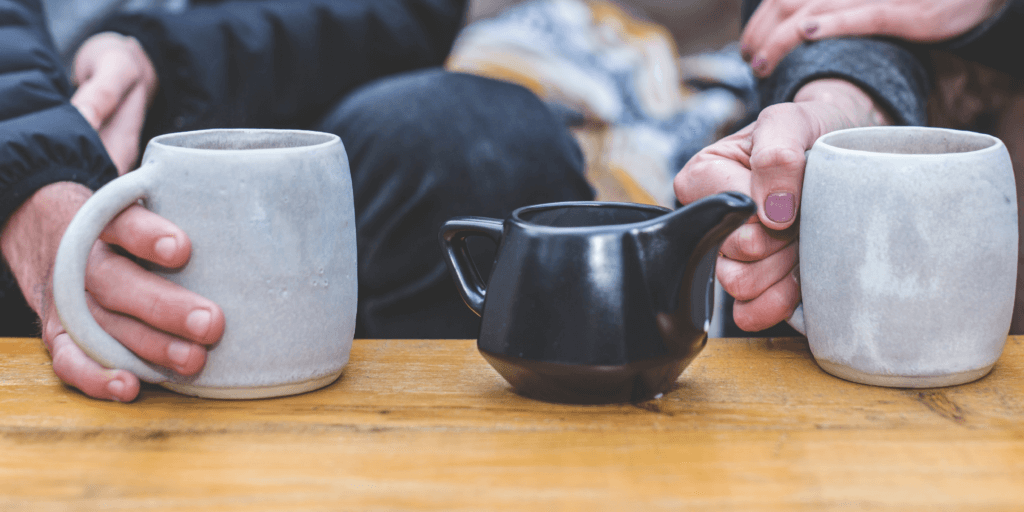 Close-up van drie tassen op een houten tafel, met wazige mensen op de achtergrond.