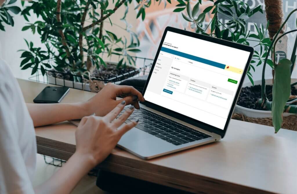 Persoon werkt op een laptop met de website mijnvaph.be open. Achter de laptop staan enkele groene planten.