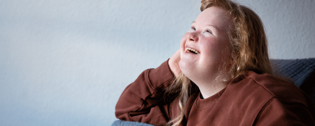 Jonge vrouw met syndroom van Down kijkt in de verte en lacht.
